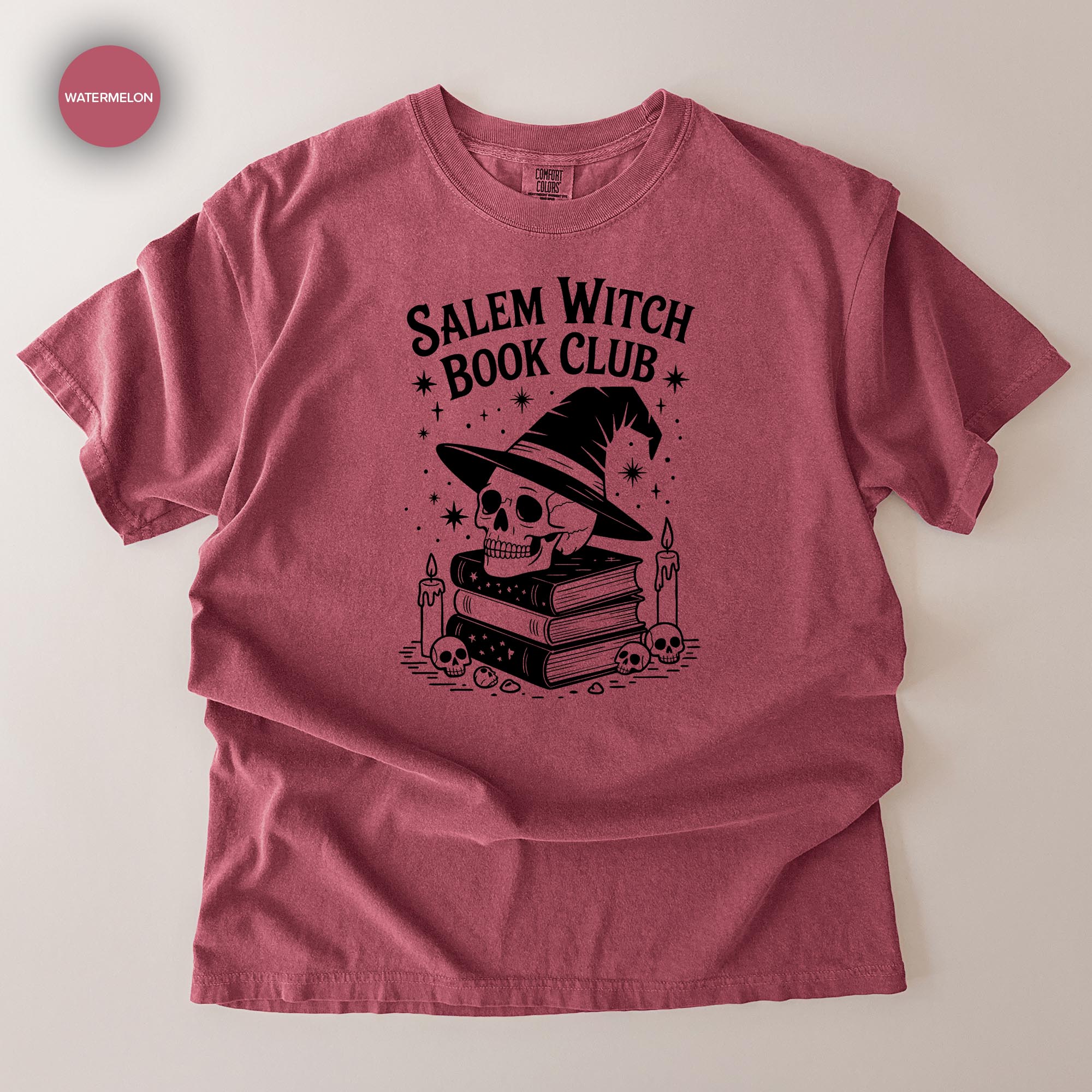 A red t-shirt with a graphic design featuring a skull wearing a witch's hat, surrounded by books and candles, with the text "Salem Witch Book Club" printed on it.