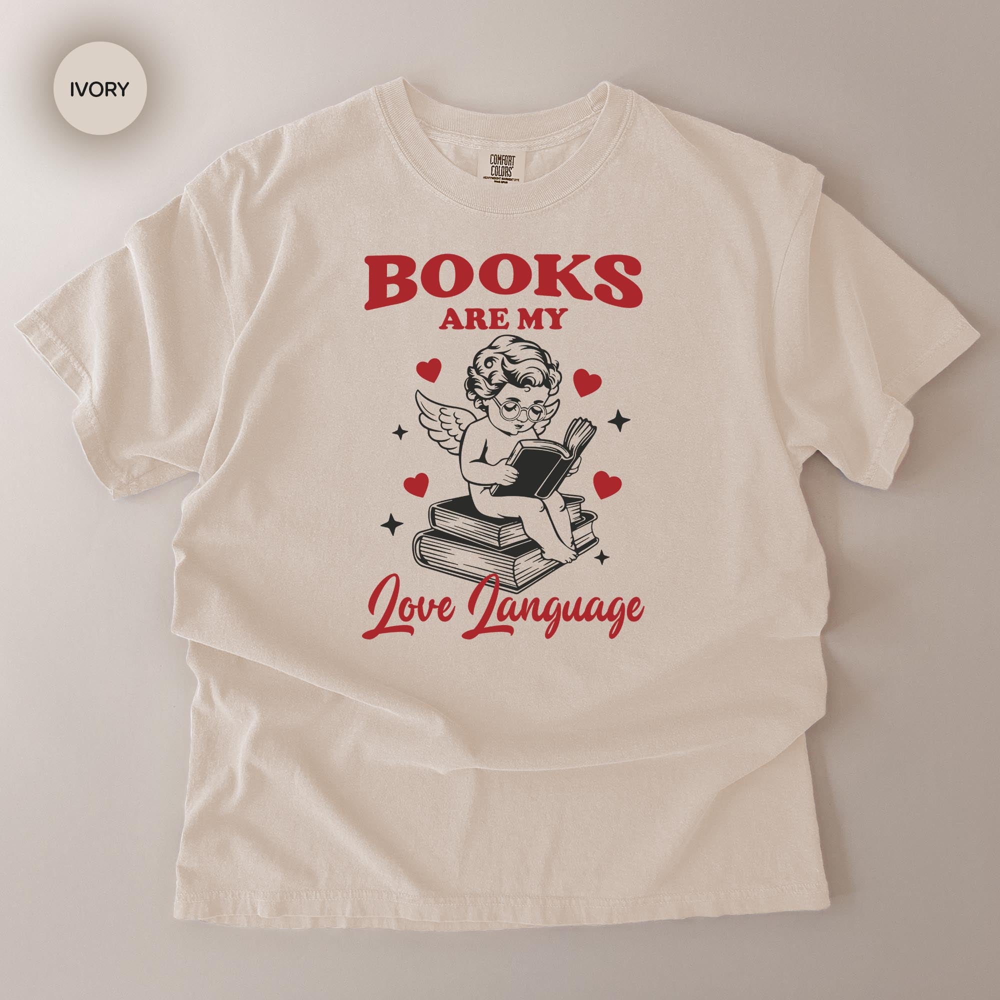 A white t-shirt with a graphic design featuring a cherub holding a book and surrounded by hearts, along with the text "BOOKS ARE MY LOVE LANGUAGE".