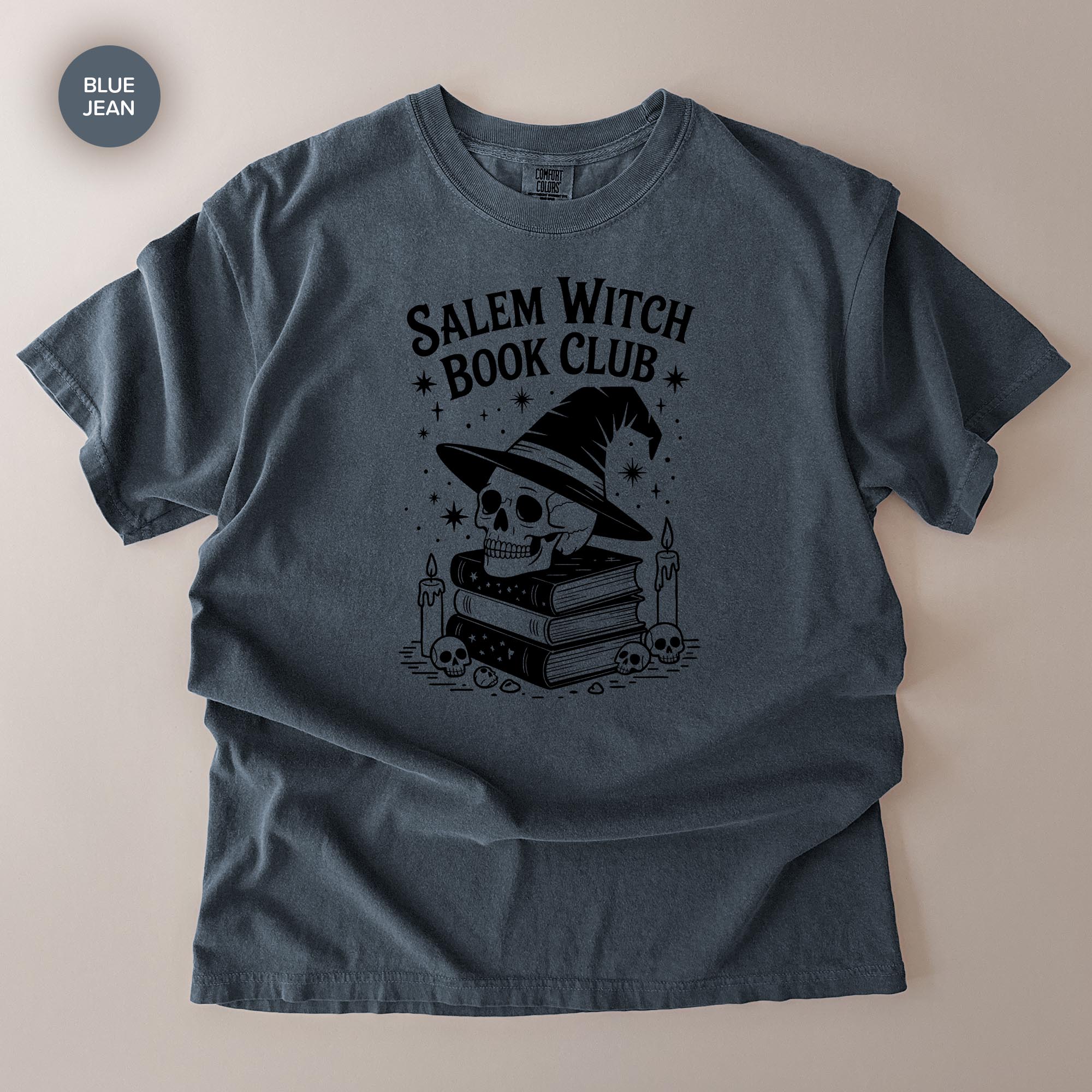 A gray t-shirt with a graphic design featuring a skull wearing a witch's hat, surrounded by books and candles, with the text "Salem Witch Book Club" printed on it.