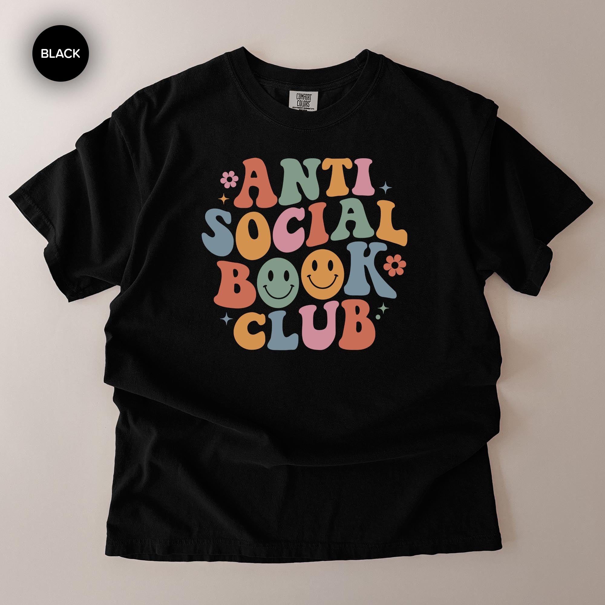 A black t-shirt with a colorful graphic design that says "ANTI SOCIAL BOOK CLUB" in a playful, retro style.