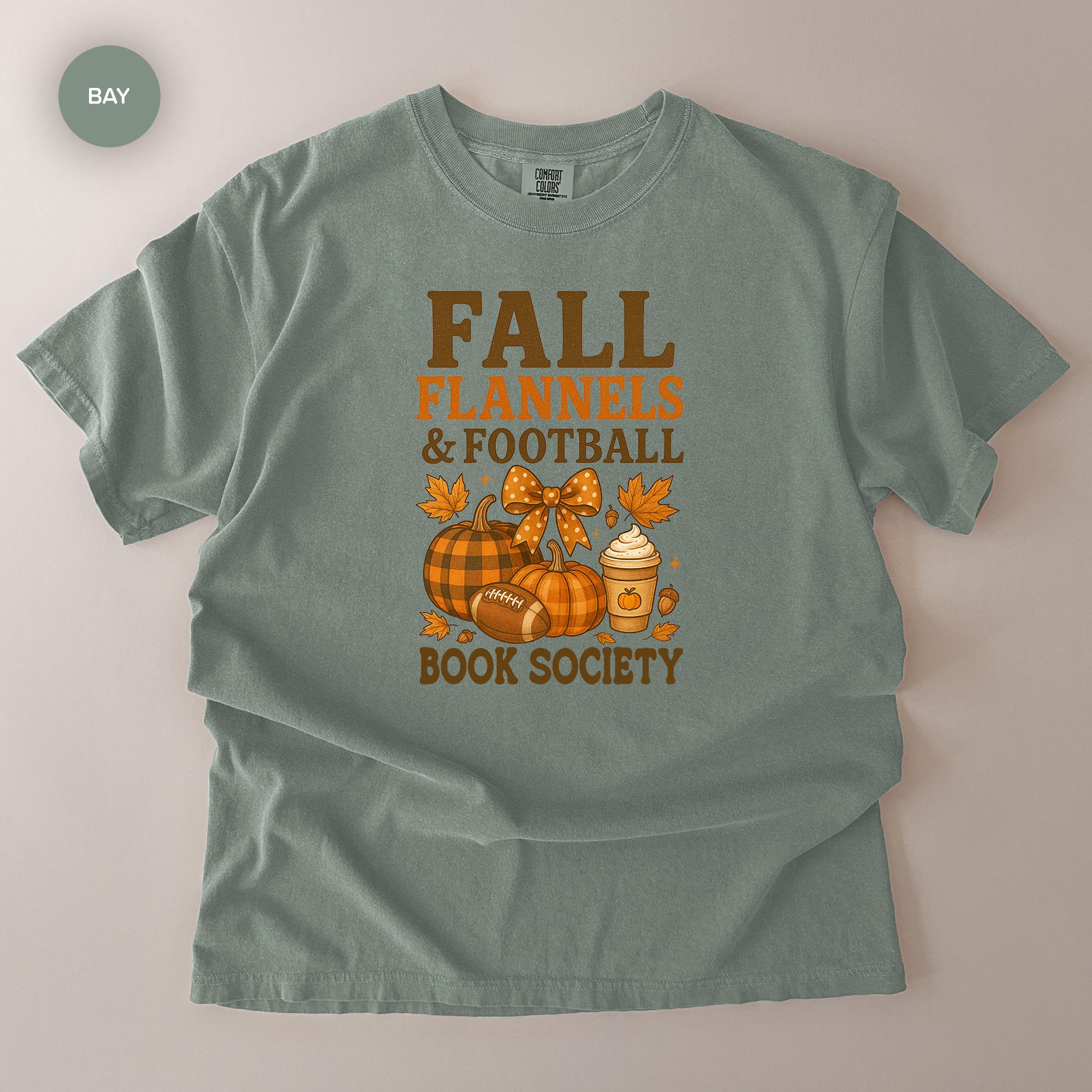 A gray t-shirt with a graphic design featuring fall-themed elements such as pumpkins, a football, and a book, along with the text "FALL FLANNELS & FOOTBALL BOOK SOCIETY".
