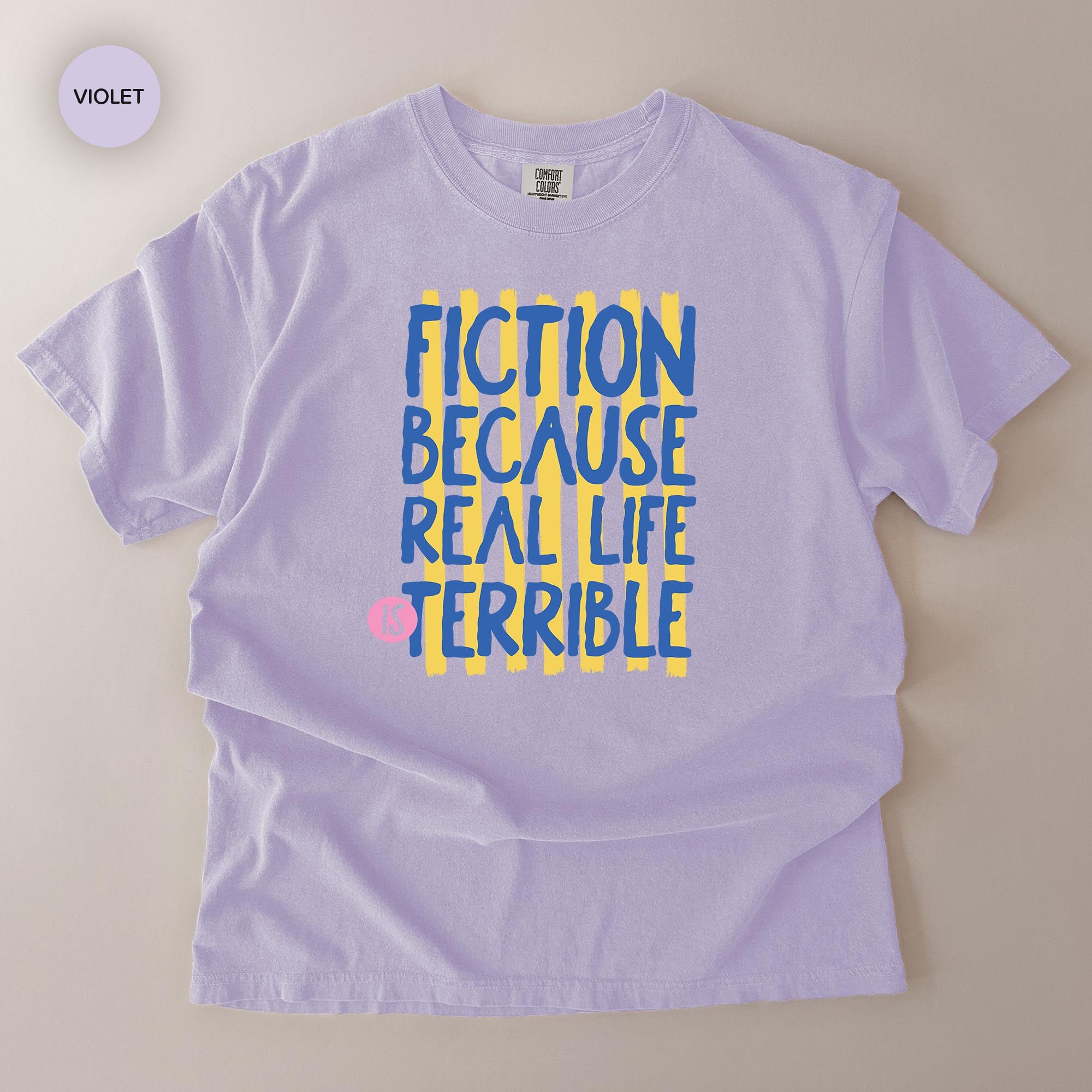 A purple t-shirt with a graphic design featuring the text "FICTION BECAUSE REAL LIFE IS TERRIBLE" in a stylized font.