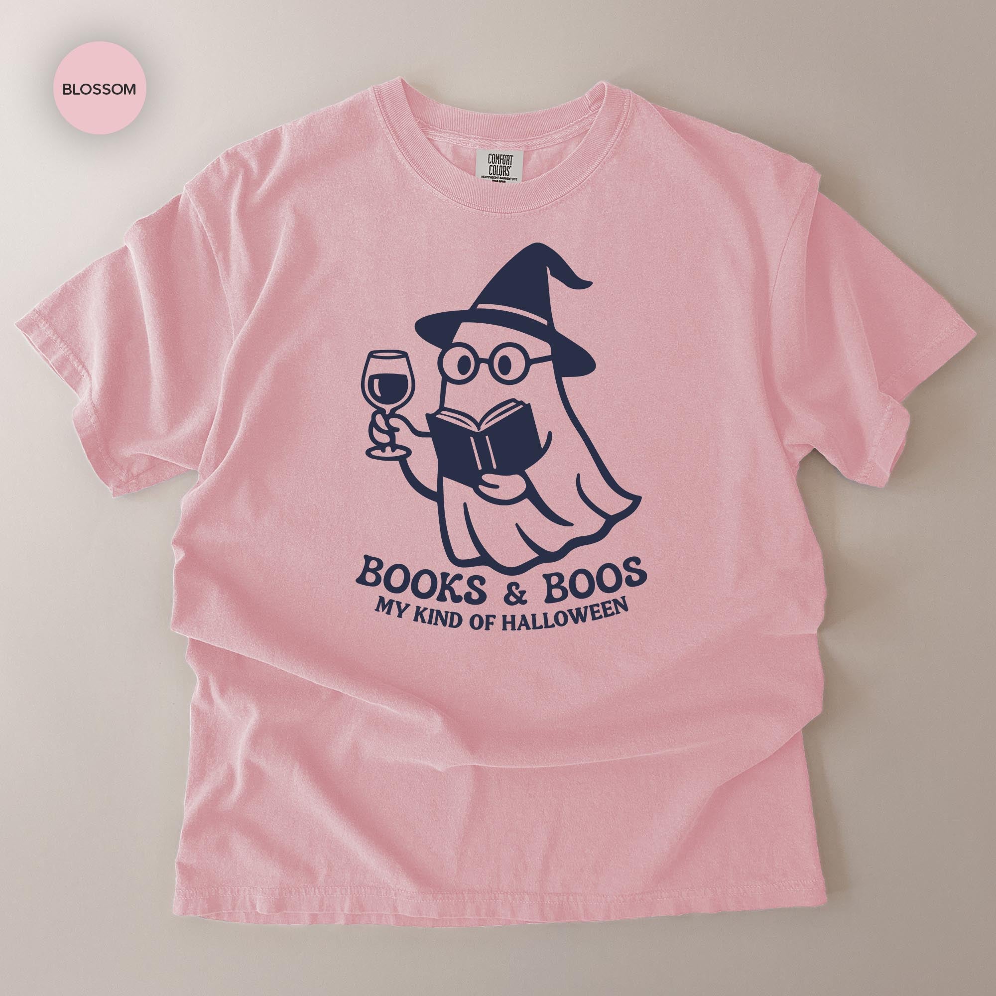 A pink t-shirt with a graphic design depicting a ghost character holding a book and a wine glass, along with the text "Books & Boo's MY KIND OF HALLOWEEN".