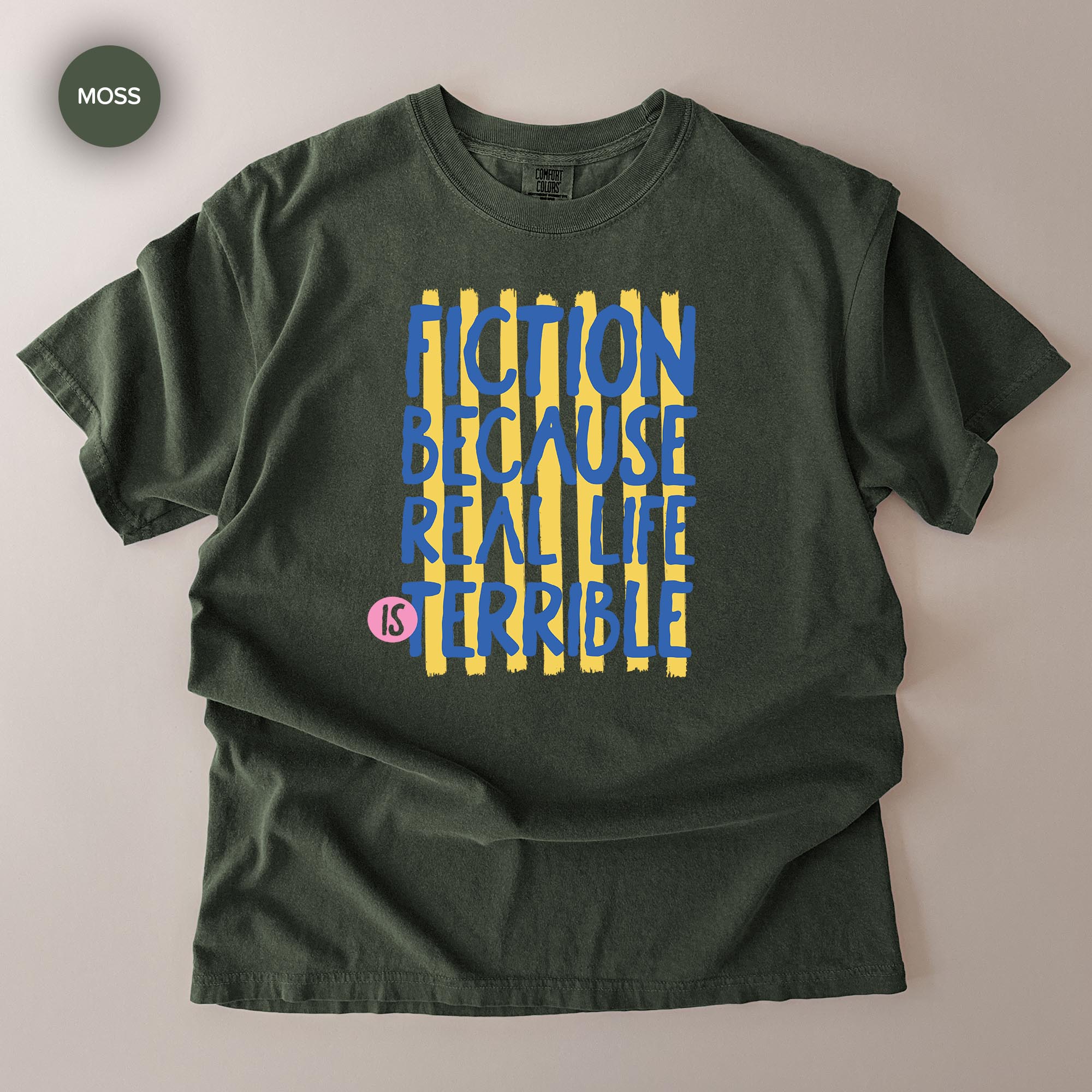A dark green t-shirt with a graphic design featuring the text "FICTION BECAUSE REAL LIFE IS TERRIBLE" in a bold, stylized font.