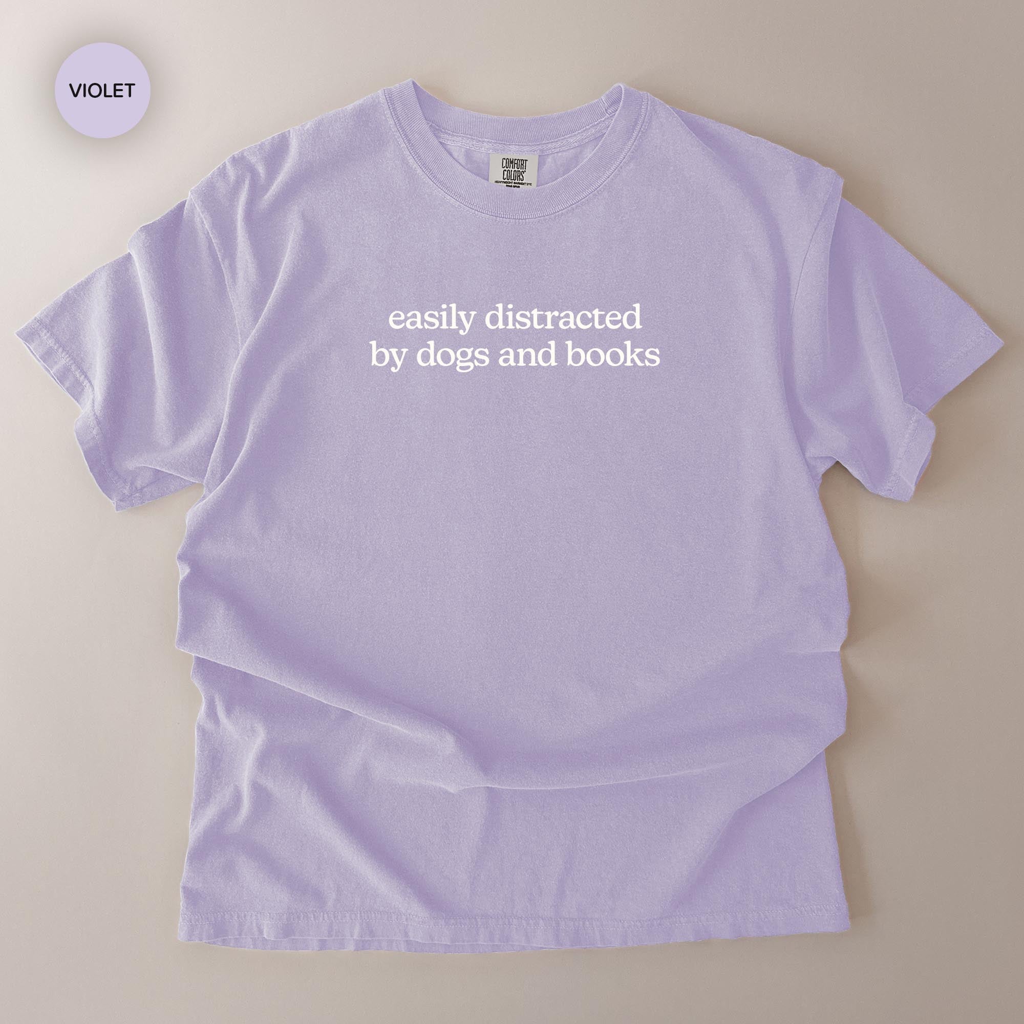 A purple t-shirt with the text "easily distracted by dogs and books" printed on it.
