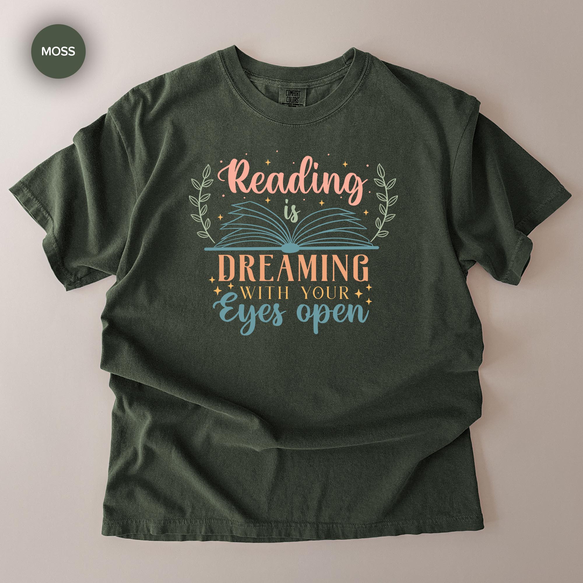 A green t-shirt with a printed design that says "Reading is Dreaming with your eyes open".