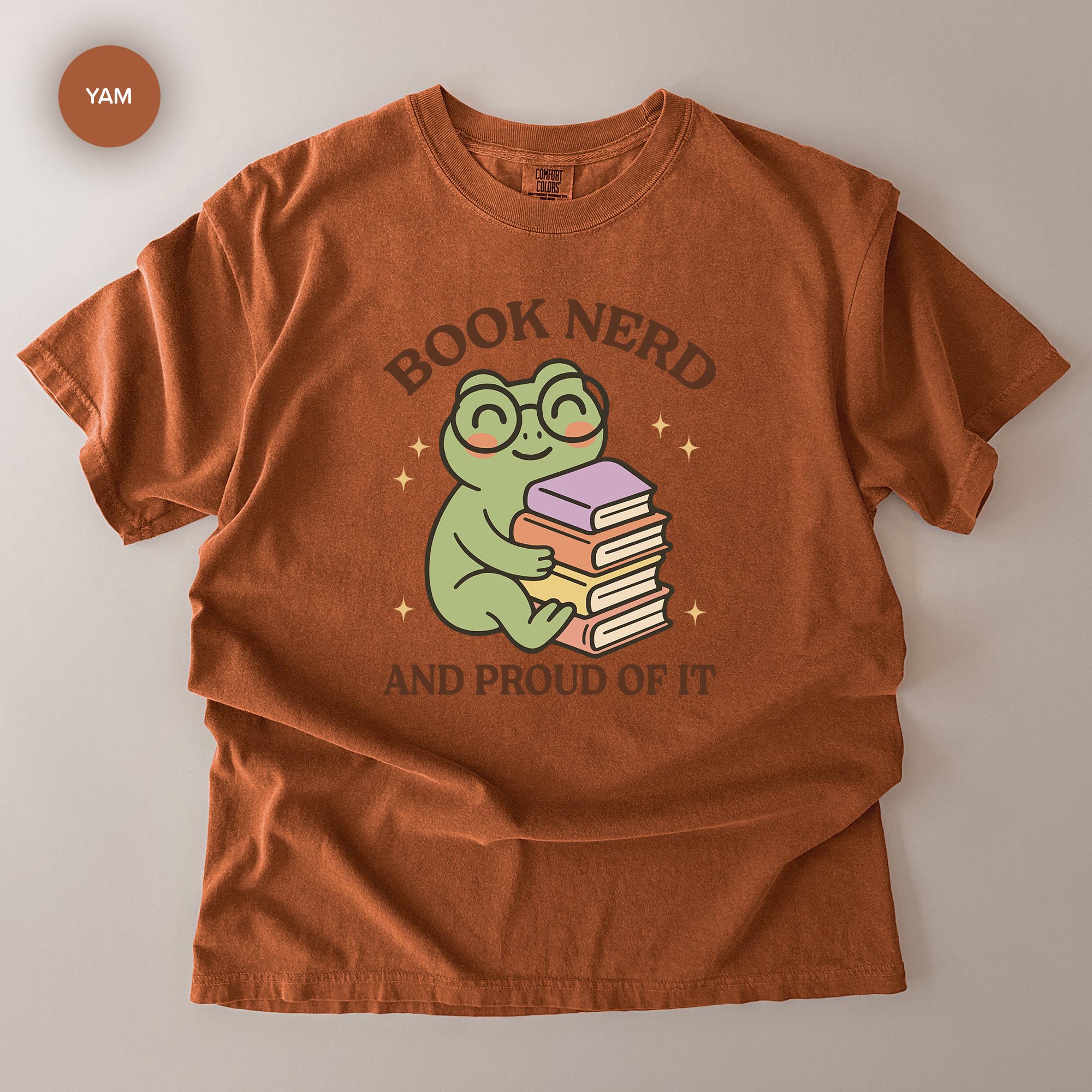 a red t-shirt with a cartoon frog wearing glasses and holding a stack of books. The text on the t-shirt reads "BOOK NERD AND PROUD OF IT".