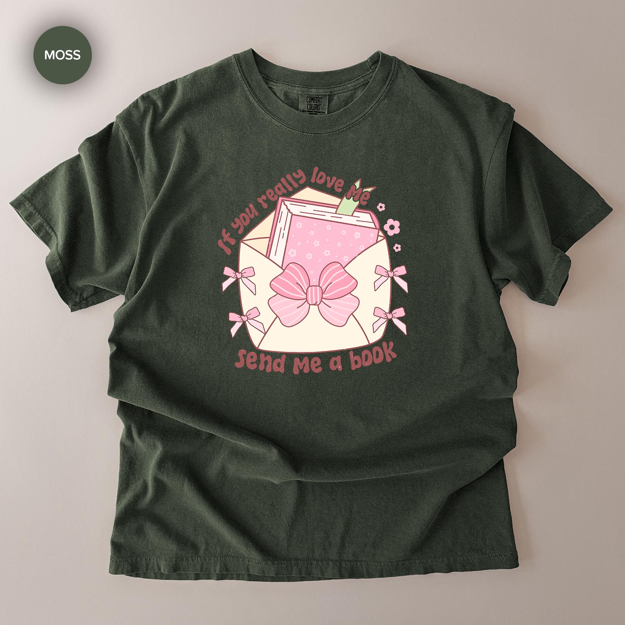 A green t-shirt with a graphic design featuring a pink bow, a book, and the text "If you really love me, send me a book".