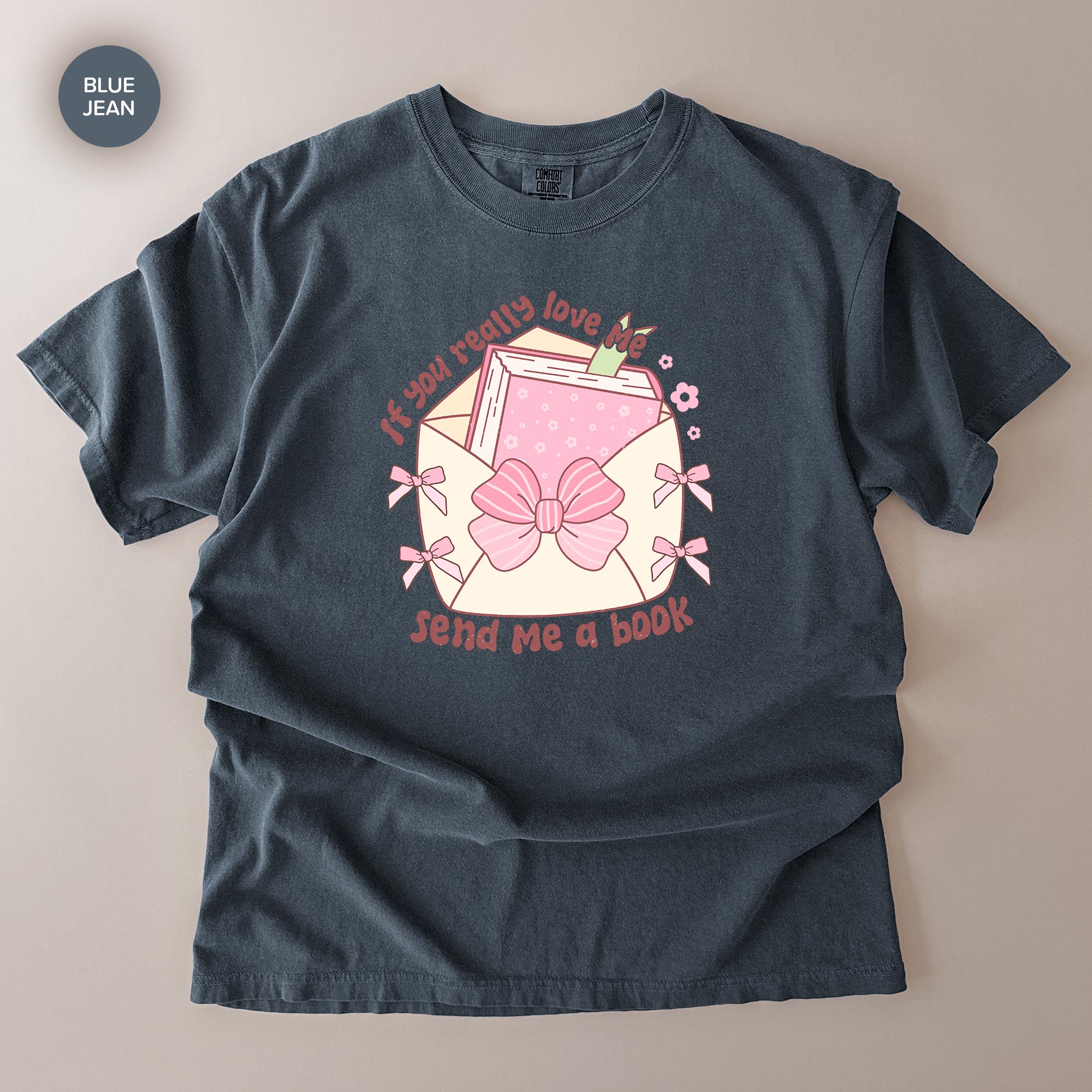 A gray t-shirt with a graphic design featuring a pink bow, a book, and the text "If you really love me, send me a book".