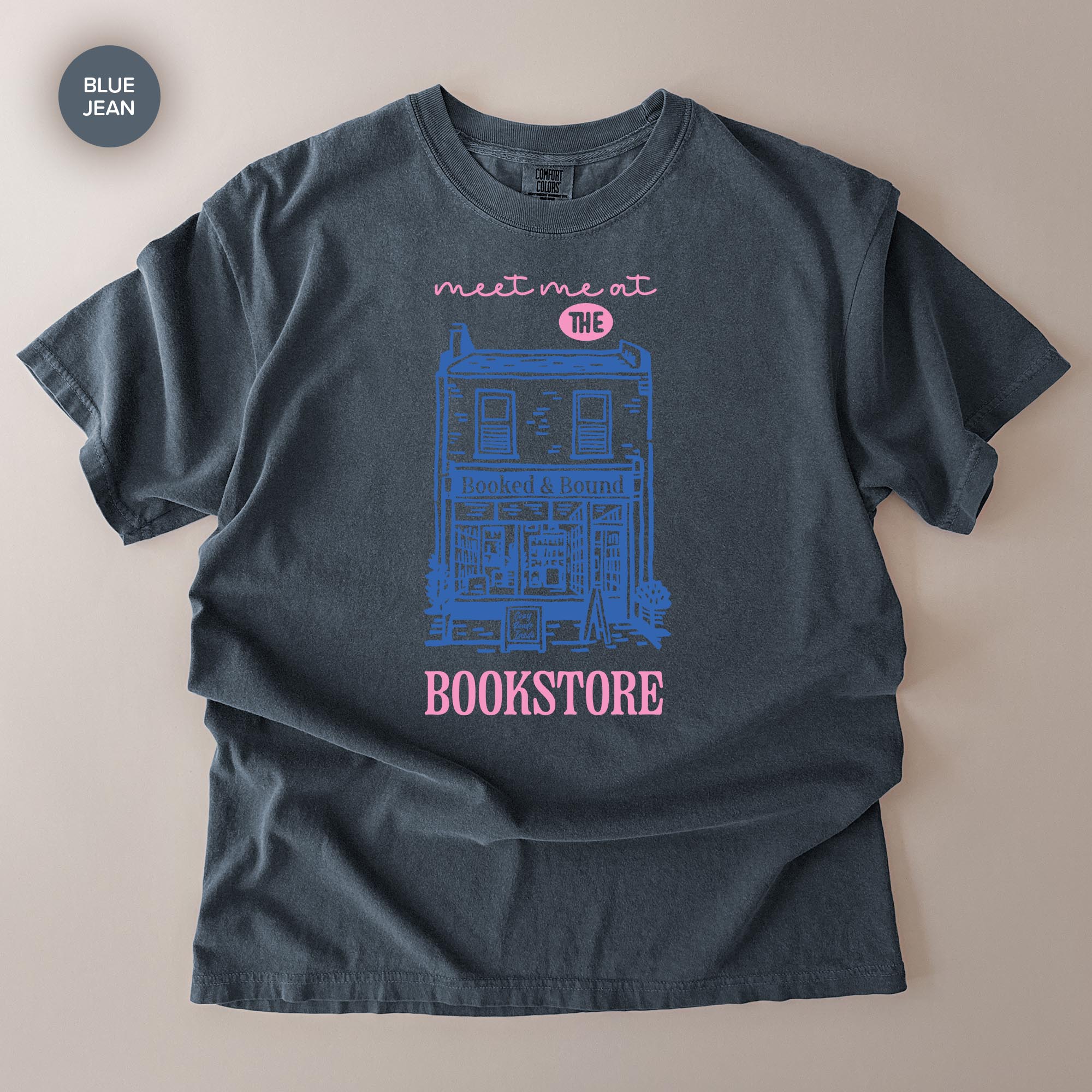 A gray t-shirt with a graphic design depicting a building and the text "Meet me at the BOOKSTORE" printed on it.
