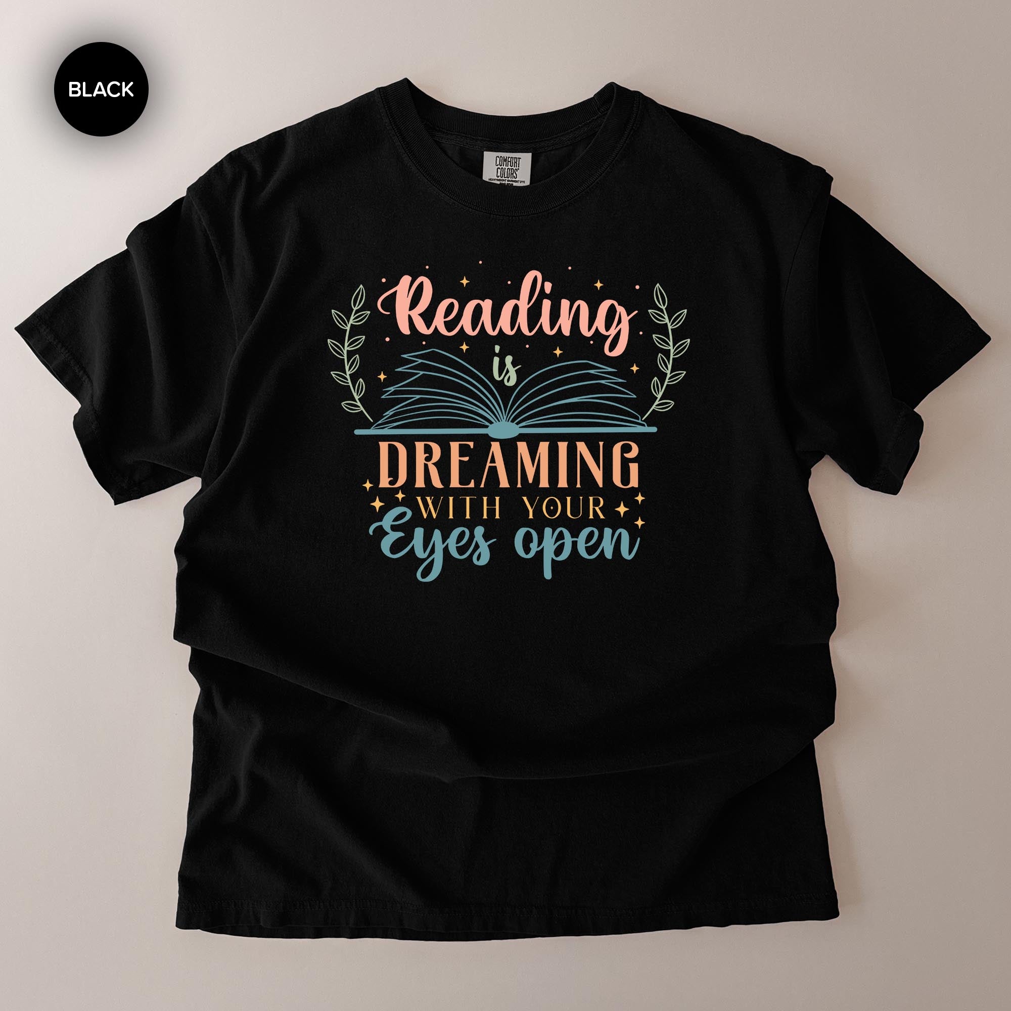 A black t-shirt with a colorful graphic design that says "Reading is Dreaming with your eyes open".