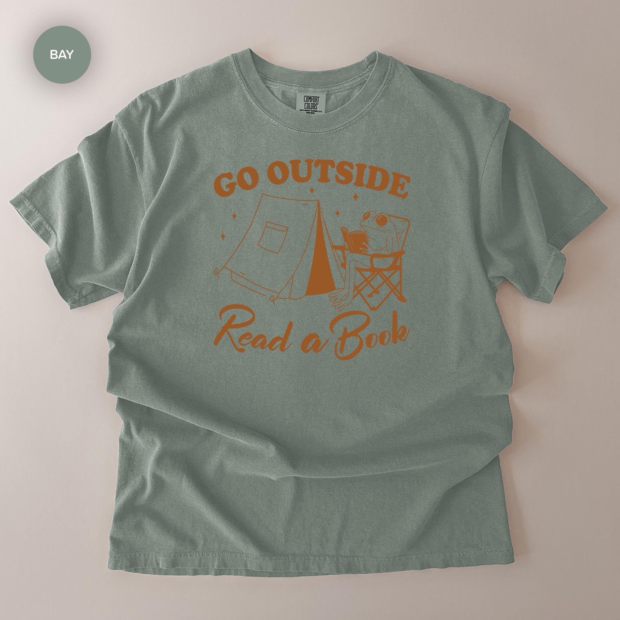 A gray t-shirt with an orange graphic design that says "Go Outside Read a Book" and features a camping scene with a tent and a person sitting in a chair.