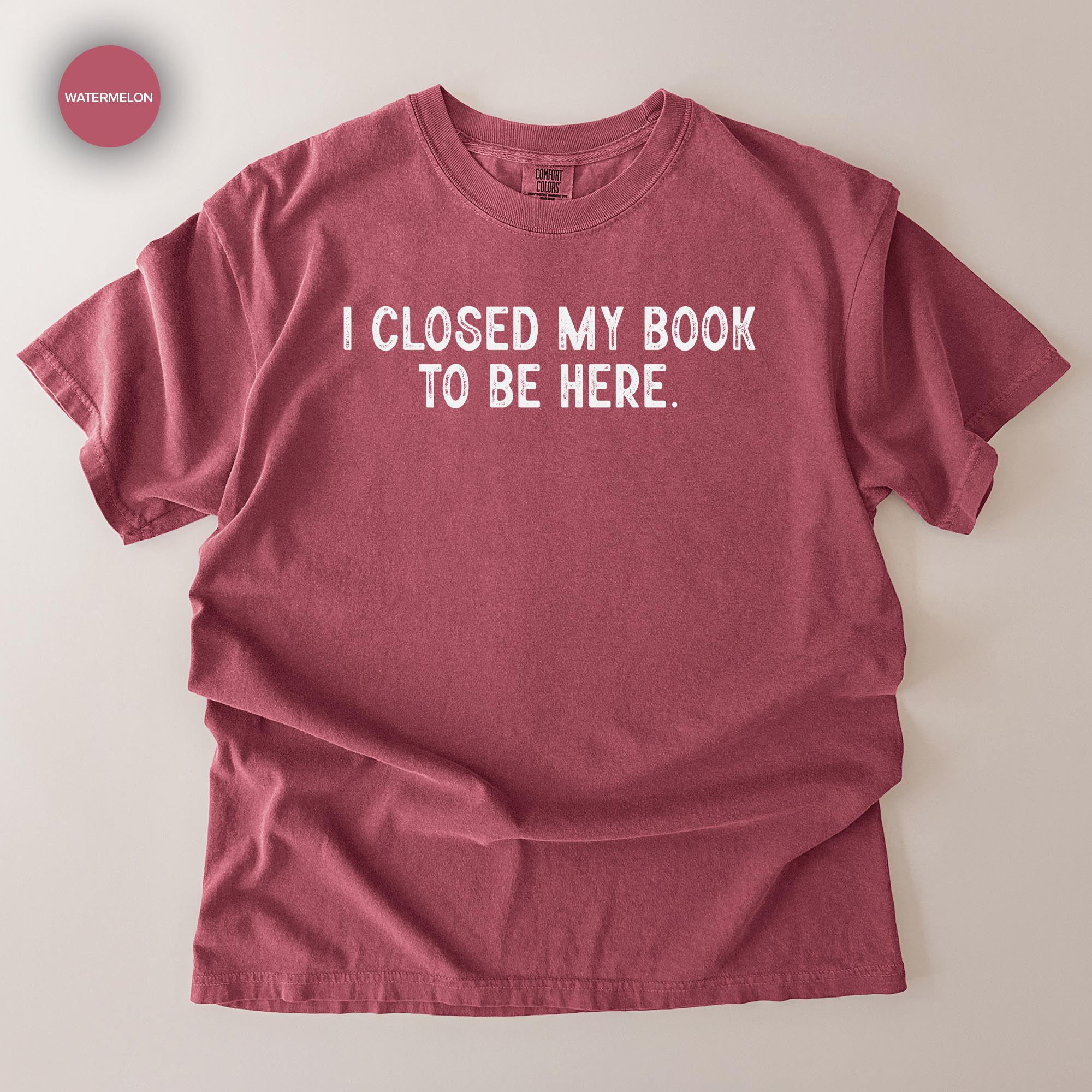 A red t-shirt with the text "I CLOSED MY BOOK TO BE HERE" printed on it.
